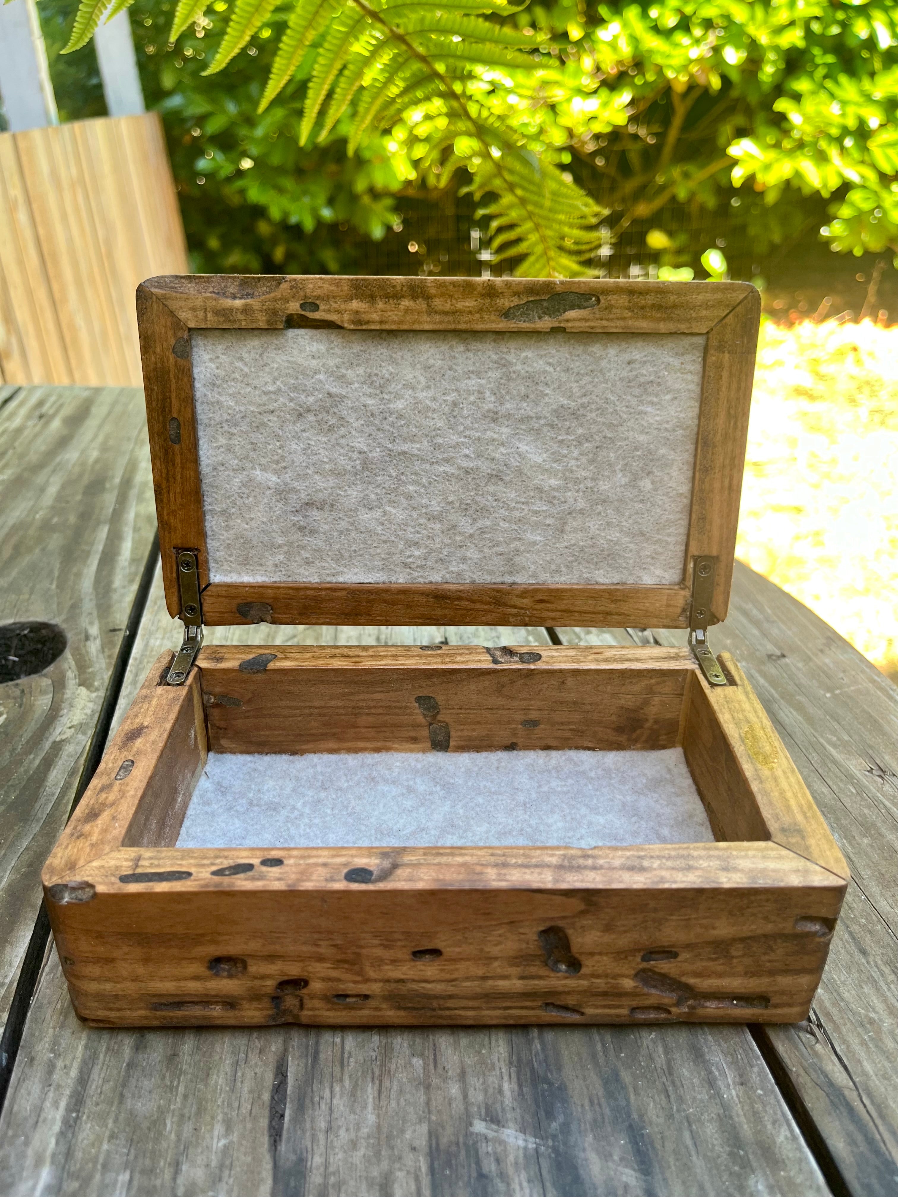 An open rustic wooden jewelry box with a light gray felt lining, placed on a weathered wooden table with a garden background. Ash wood is locally grown, lid is topped with a piece of driftwood from the Oregon coast
