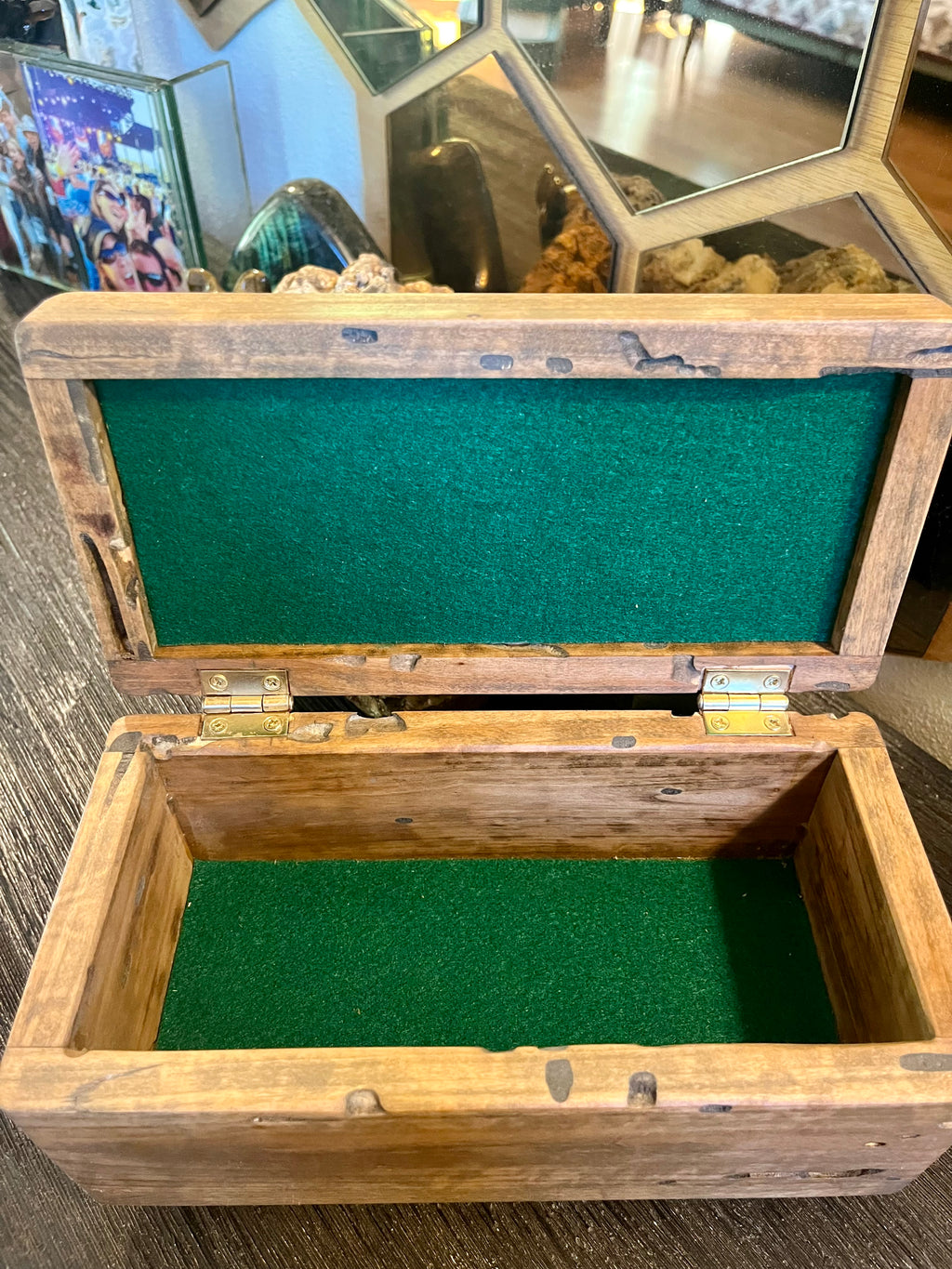 A rustic wooden jewelry box with a hinged lid, featuring a green felt lining inside, shown open on a dark wooden surface.
