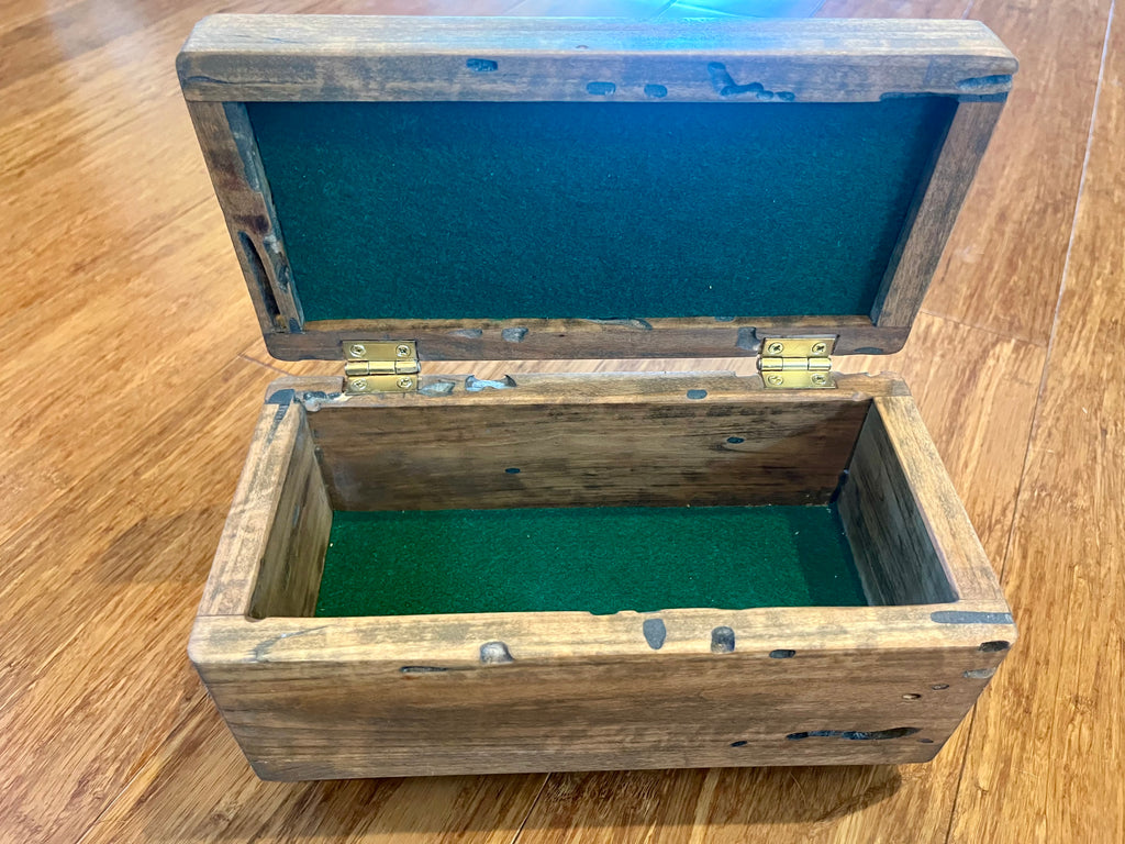 A rustic wooden storage box with an open lid, featuring a dark green felt lining inside and brass hinges, placed on a wooden floor.
