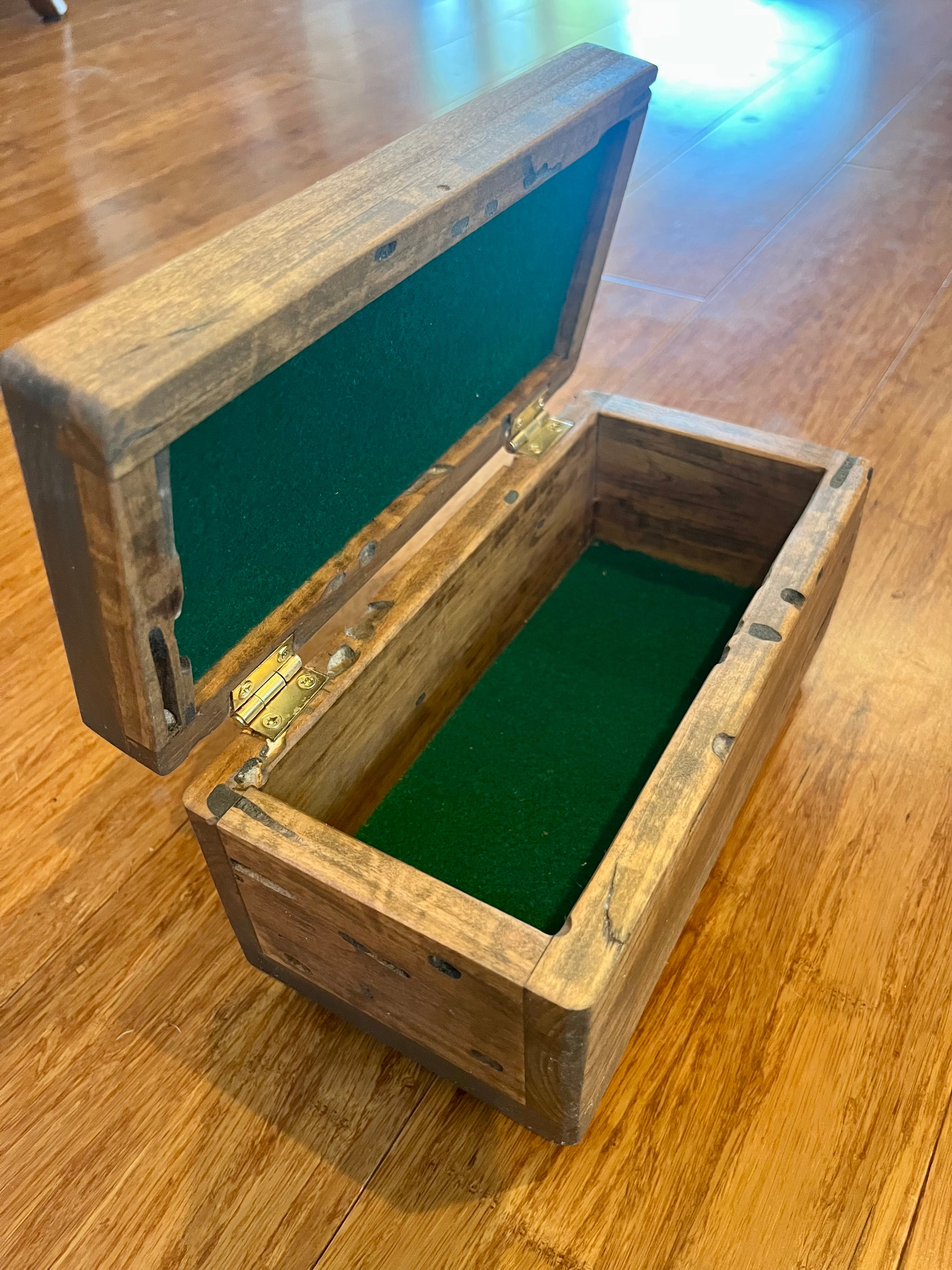 A rustic Ash wooden storage box with an open lid and brass hinges, featuring green felt lining inside, placed on a polished wooden floor. Very unique wood grain patterns.